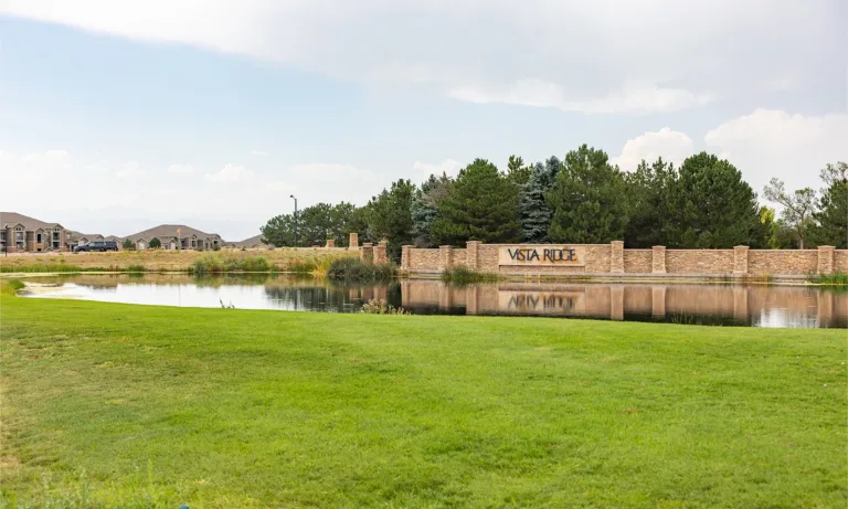 Vista Ridge community entrance beside a pond, with a stone sign, homes, trees, and landscaped lawn