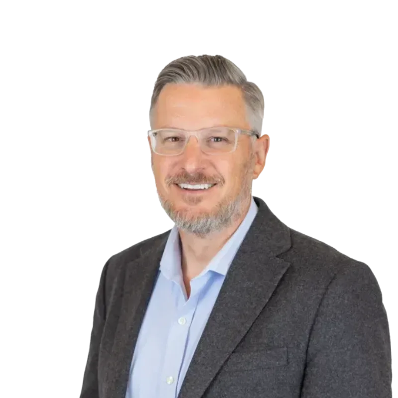Smiling middle-aged man with glasses and gray beard wearing a dark blazer and light blue shirt
