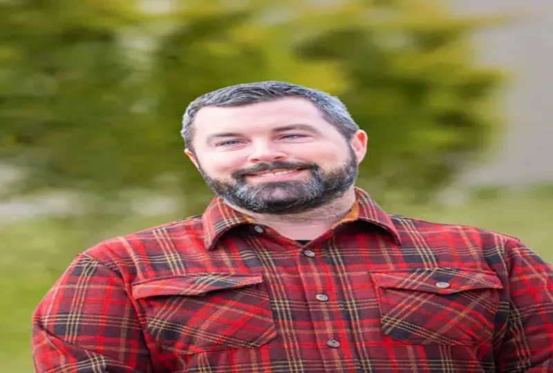 Bearded man smiling outdoors in a red plaid shirt