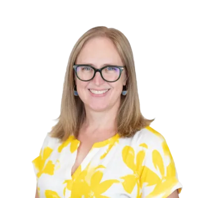 Smiling woman wearing glasses, blue earrings, and a white blouse with a yellow floral pattern