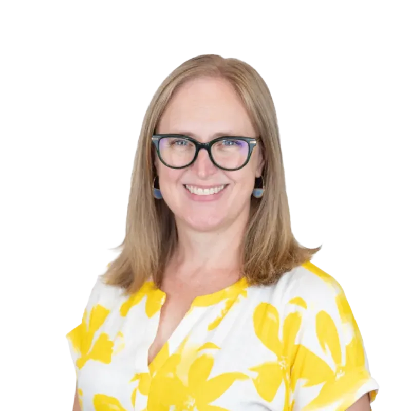 Smiling woman wearing glasses, blue earrings, and a white blouse with a yellow floral pattern