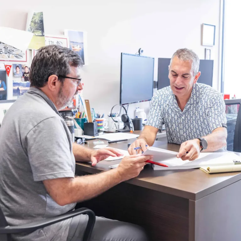 Two colleagues discuss plans and review documents together at an office desk