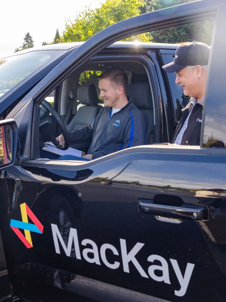 A driving instructor coaches a learner in a MacKay-branded pickup truck