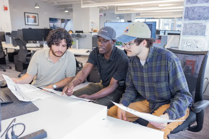 Three colleagues review architectural plans together in an office
