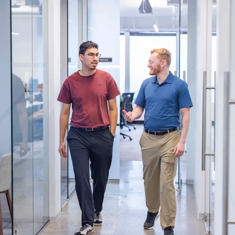 Two men walk and talk together in a bright, modern office hallway