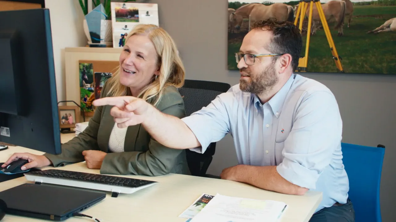 Two colleagues review a computer screen, with one pointing at it while the other uses the mouse