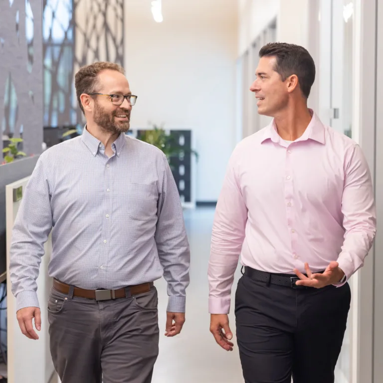 Two colleagues smiling and talking while walking through a bright office