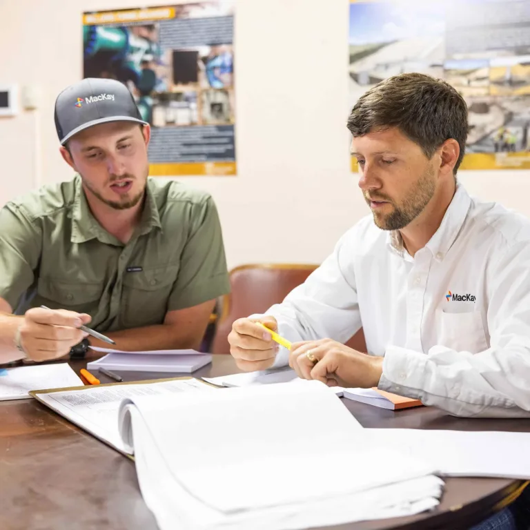 Two Mackay employees review documents and plans at a table