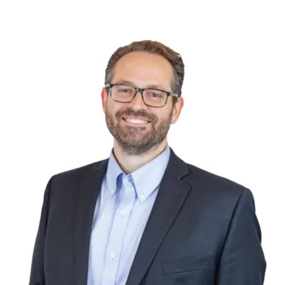 Smiling bearded man wearing glasses, a light blue shirt, and dark blazer