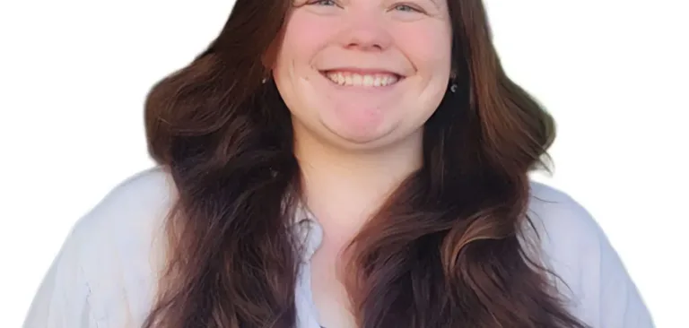 Smiling woman with long brown hair wearing a white coat over a blue shirt