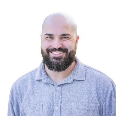 Smiling bald man with a full beard wearing a light blue collared shirt