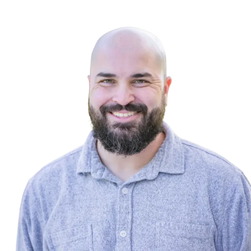 Smiling bald man with a full beard wearing a light blue collared shirt