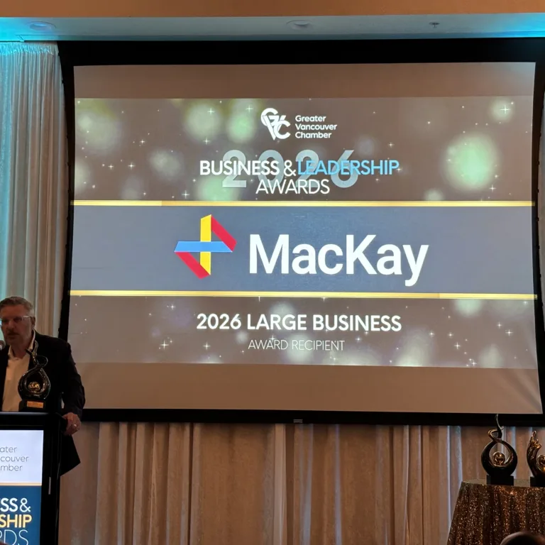 Man holding an award at a podium beside a screen naming Mackay the 2026 Large Business Award recipient