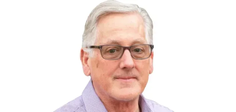 Middle-aged man with gray hair and glasses wearing a purple checkered shirt