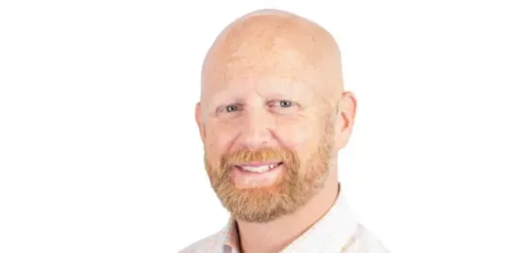 Portrait of a smiling bald man with a reddish beard wearing a light plaid shirt