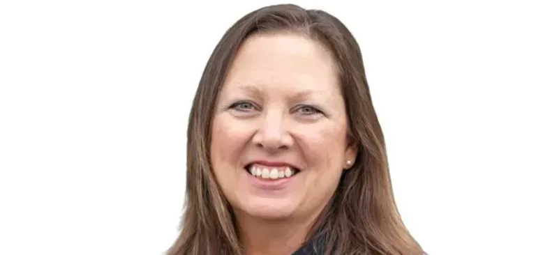 Smiling woman with shoulder-length brown hair wearing a dark blouse and pearl necklace